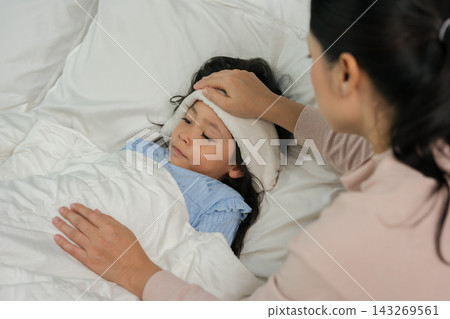 mother applying cold compress on sick daughter's forehead in bed mother applying cold compress on sick daughter's forehead in bed 143269561
