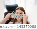 Doctor holding optical trial lens frame for teenage girl 143270068
