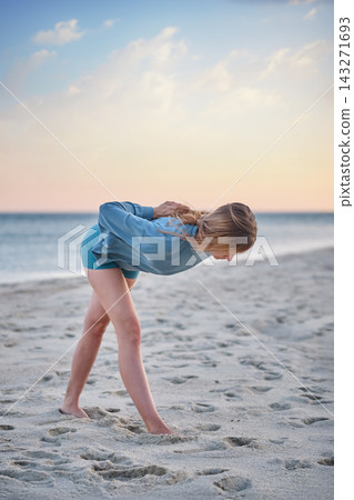 With her torso held nearly horizontal, a woman practices a Parsvottanasana yoga variation, Pyramid Pose, with reverse-prayer hands on a sandy beach With her torso held nearly horizontal, a woman practices a Parsvottanasana yoga variation, Pyramid Pose, with reverse-prayer hands on a sandy beach 143271693