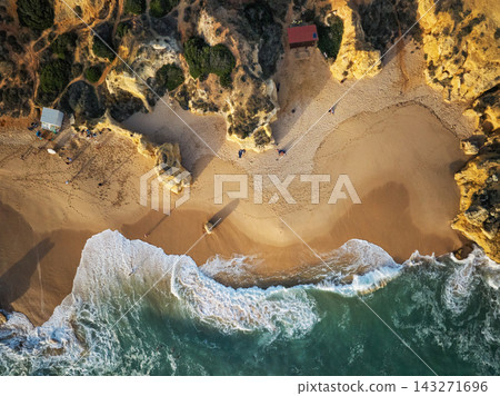 Drone top down view of Praia de Sao Rafael beach with a sandy cove, white surf, and rugged golden cliffs. Drone top down view of Praia de Sao Rafael beach with a sandy cove, white surf, and rugged golden cliffs. 143271696
