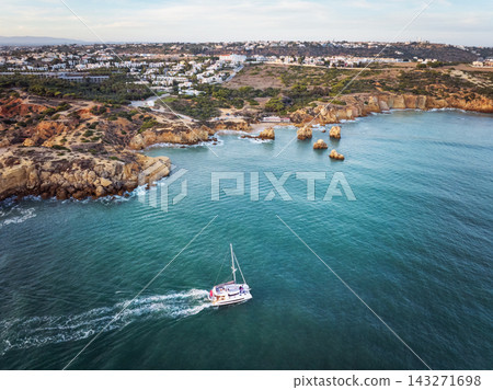 Aerial view of Praia dos Arrifes in warm evening light with golden cliffs, rocky islets and green Atlantic water. Aerial view of Praia dos Arrifes in warm evening light with golden cliffs, rocky islets and green Atlantic water. 143271698