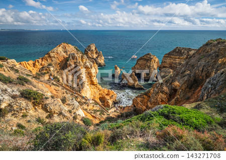 View from the clifftop path at Ponta da Piedade in Lagos, Algarve, Portugal, with golden limestone sea stacks, turquoise water and a wooden staircase leading down to the cove. View from the clifftop path at Ponta da Piedade in Lagos, Algarve, Portugal, with golden limestone sea stacks, turquoise water and a wooden staircase leading down to the cove. 143271708