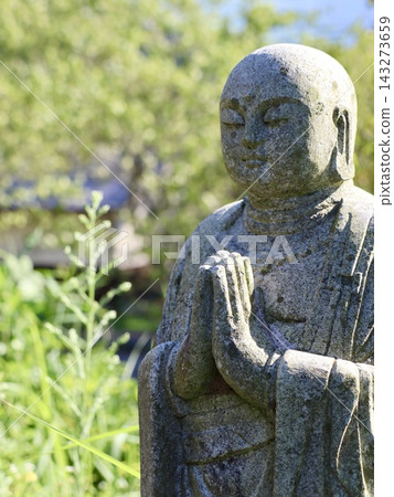 A stone statue of a Japanese Jizo (guardian deity) with a serene expression and clasped hands amidst greenery | Suitable for books, articles, and web advertisements conveying Japanese culture and prayer. A stone statue of a Japanese Jizo (guardian deity) with a serene expression and clasped hands amidst greenery | Suitable for books, articles, and web advertisements conveying Japanese culture and prayer. 143273659