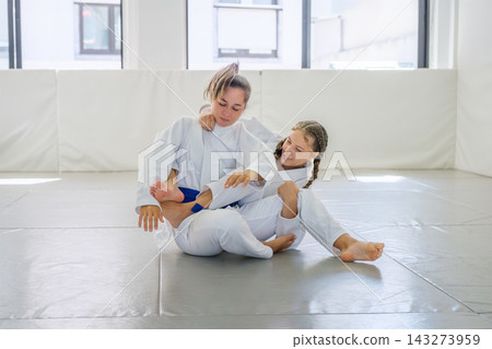 Two Brazilian jiu jitsu students practice a bow and arrow choke setup as one holds the collar and pants near the knee while leaning sideways 143273959