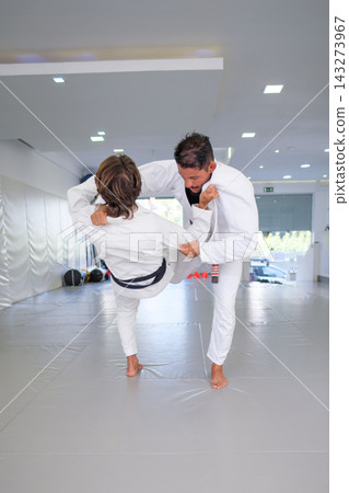 Male martial artists demonstrate the entry to uchi-mata, the judo inner thigh reaping throw, during Brazilian jiu jitsu (BJJ) practice with a raised attacking leg Male martial artists demonstrate the entry to uchi-mata, the judo inner thigh reaping throw, during Brazilian jiu jitsu (BJJ) practice with a raised attacking leg 143273967
