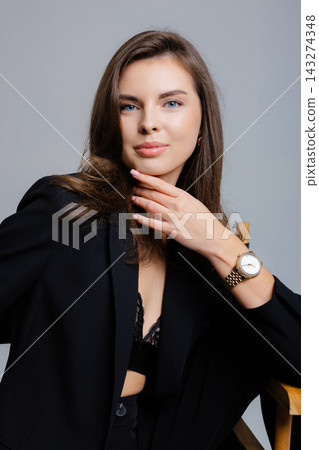 Elegant businesswoman posing with hand on chin wearing black jacket and wristwatch 143274348