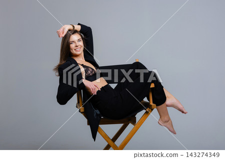 Young businesswoman posing on director chair wearing black suit and lace bra 143274349