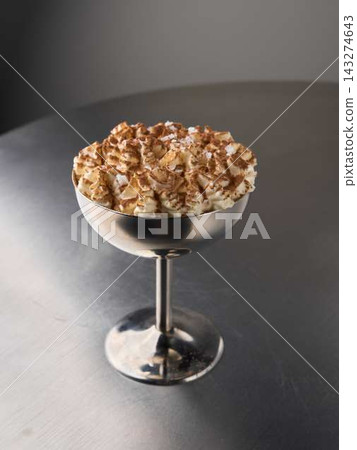 Close-up creamy whipped cream dessert in metal pedestal bowl, topped with cocoa dust and coconut flakes on reflective stainless steel table Close-up creamy whipped cream dessert in metal pedestal bowl, topped with cocoa dust and coconut flakes on reflective stainless steel table 143274643