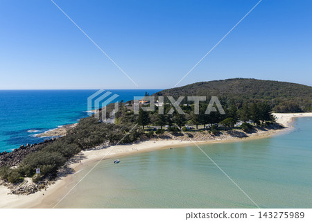 An aerial view of Laggers Point surrounded by clear turquoise ocean, with the historic Trial Bay Gaol visible in the background. This coastal landmark lies within Arakoon National Park An aerial view of Laggers Point surrounded by clear turquoise ocean, with the historic Trial Bay Gaol visible in the background. This coastal landmark lies within Arakoon National Park 143275989