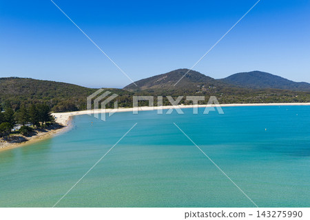 Aerial view of the expansive sandy shoreline and clear turquoise water of Front Beach, with coastal vegetation and mountains rising in the background near South West Rocks, New South Wales, Australia Aerial view of the expansive sandy shoreline and clear turquoise water of Front Beach, with coastal vegetation and mountains rising in the background near South West Rocks, New South Wales, Australia 143275990