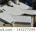 Warm roof under the snow. Corrugated roof blanketed in snow with three weathered chimneys and visible vents. Late winter sunlight creates soft shadows and detailed ice texture for upkeep visuals. 143277299