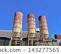 Three Weathered Silos On Lattice Legs Against Blue Sky Three Weathered Silos On Lattice Legs Against Blue Sky 143277565