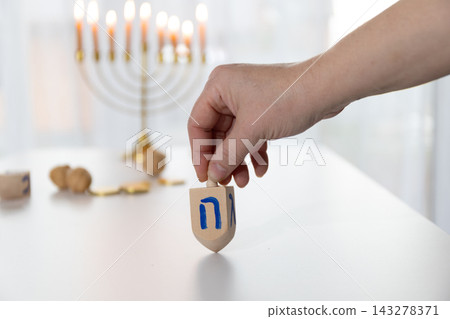Hand Holding a Wooden Dreidel Poised to Spin in Hanukkah Scene Hand Holding a Wooden Dreidel Poised to Spin in Hanukkah Scene 143278371