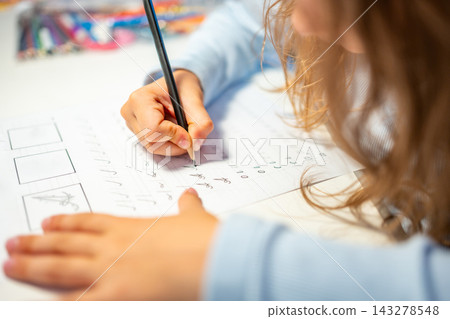 First grade girl practices handwriting with pencil in school workbook. Child learns to write letters during early education with selective focus and shallow depth of field First grade girl practices handwriting with pencil in school workbook. Child learns to write letters during early education with selective focus and shallow depth of field 143278548