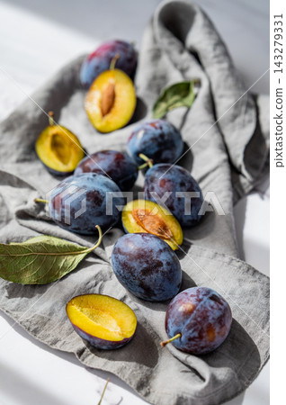Fresh blue plum whole and sliced on a napkin with green leaves on marble background with sunlight. 143279331