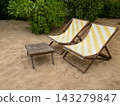 Yellow striped beach deck chairs and wooden table on sand 143279847