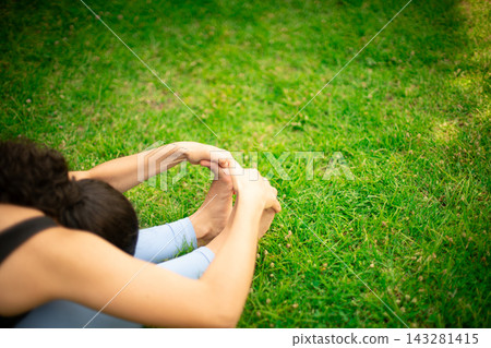 Woman practicing yoga stretching forward bend outdoors on grass 143281415