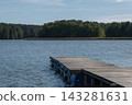 A wooden pier juts out into a calm lake, with a forest in the background 143281631