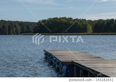 A wooden pier juts out into a calm lake, with a forest in the background A wooden pier juts out into a calm lake, with a forest in the background 143281631