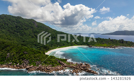 Green hills overlooking a white sandy beach with turquoise ocean waves and blue sky. Petite Anse. Seychelles, La Digue. Green hills overlooking a white sandy beach with turquoise ocean waves and blue sky. Petite Anse. Seychelles, La Digue. 143281926