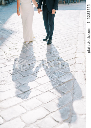 Couple holding hands on sunlit cobblestone street Couple holding hands on sunlit cobblestone street 143283853