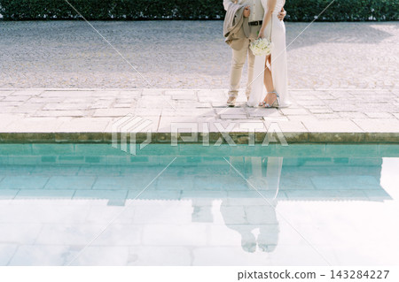 Elegant wedding couple standing by poolside Elegant wedding couple standing by poolside 143284227
