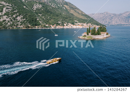 Swift speedboat rushes by tiny church island amid scenic mountain backdrop and calm waters 143284267