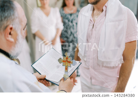 Priest Holding Cross and Book During Religious Ceremony Priest Holding Cross and Book During Religious Ceremony 143284380