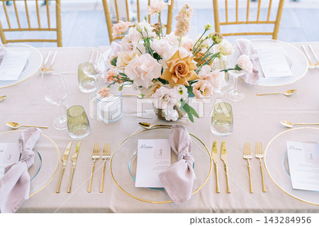 Chic pastel dining arrangement. Refined pastel reception display with elegant tableware and soft illumination Chic pastel dining arrangement. Refined pastel reception display with elegant tableware and soft illumination 143284956