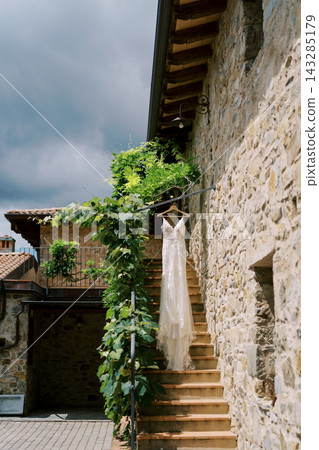 Charming wedding dress gracefully draped on rustic stone steps under leafy balcony canopy Charming wedding dress gracefully draped on rustic stone steps under leafy balcony canopy 143285179