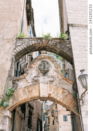 Old archway scene. Timeworn stone arch crosses compact historic street scene with peeling walls Old archway scene. Timeworn stone arch crosses compact historic street scene with peeling walls 143285233