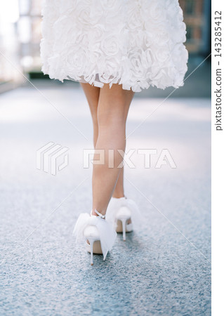 Bride in stylish white dress and pompom skates gliding through city streets happily Bride in stylish white dress and pompom skates gliding through city streets happily 143285412