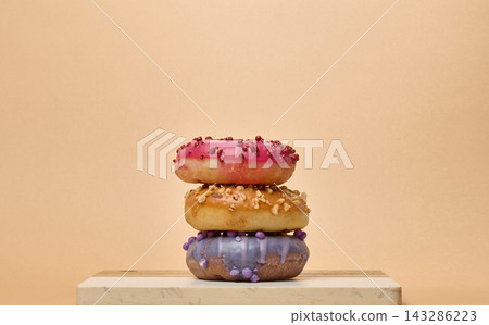 Stack of three multicolored donuts with glaze and sprinkles on a board Stack of three multicolored donuts with glaze and sprinkles on a board 143286223