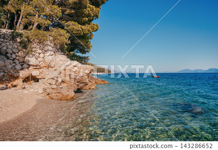 Scenic coastal view featuring clear turquoise water, rocky shoreline, and lush green trees under a bright blue sky in a serene natural environment Scenic coastal view featuring clear turquoise water, rocky shoreline, and lush green trees under a bright blue sky in a serene natural environment 143286652