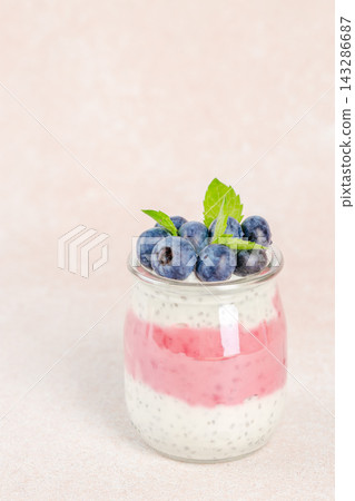 Layered yogurt dessert in a glass jar with chia seeds, topped with fresh blueberries and mint leaves against a soft pink background. copy space Layered yogurt dessert in a glass jar with chia seeds, topped with fresh blueberries and mint leaves against a soft pink background. copy space 143286687