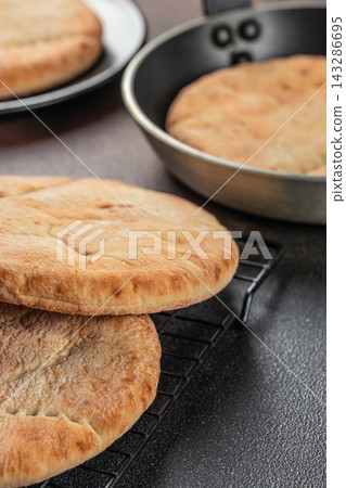 Freshly baked round flatbreads stacked on a cooling rack beside a metal baking pan and plated bread in a warm kitchen close up Freshly baked round flatbreads stacked on a cooling rack beside a metal baking pan and plated bread in a warm kitchen close up 143286695