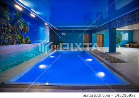 a modern large indoor pool with blue lighting and a waterfall. 143286952