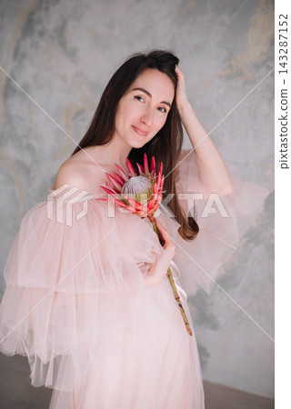 Elegant young woman and girl in pink tulle dress holding a protea flower Elegant young woman and girl in pink tulle dress holding a protea flower 143287152