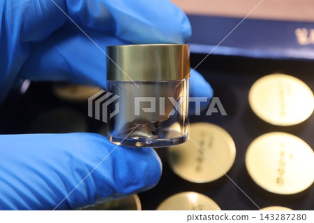 Gloved Hand Holding Cosmetic Jar with Gold Lid Gloved Hand Holding Cosmetic Jar with Gold Lid 143287280