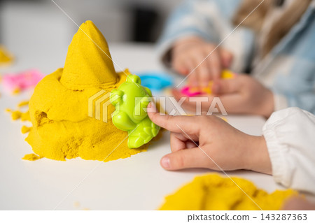 Children playing with yellow kinetic sand and colorful plastic molds Children playing with yellow kinetic sand and colorful plastic molds 143287363