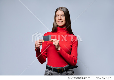 Woman in red turtleneck holding black plastic card studio shot Woman in red turtleneck holding black plastic card studio shot 143287846