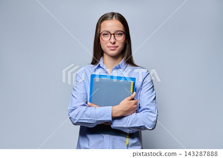 Smiling young female student holding notebooks and folders on light background Smiling young female student holding notebooks and folders on light background 143287888