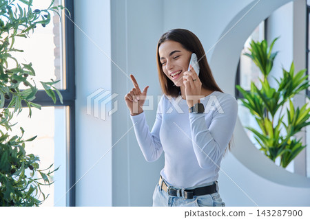 Pleasant young woman speaking on smartphone looking away indoors Pleasant young woman speaking on smartphone looking away indoors 143287900