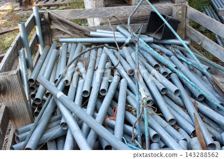Pile of galvanized and oxidized metal pipes of various sizes stacked in a rustic wooden crate outdoors, alongside a black plastic planter. Pile of galvanized and oxidized metal pipes of various sizes stacked in a rustic wooden crate outdoors, alongside a black plastic planter. 143288562