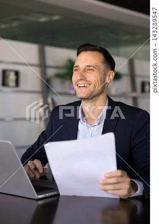 Portrait of smiling businessman sits at office desk with documents Portrait of smiling businessman sits at office desk with documents 143289547