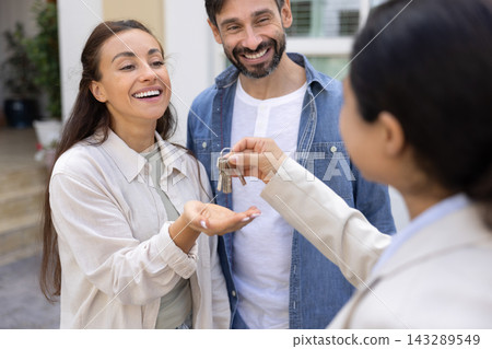 Closeup excited couple house buyers receiving home key from realtor Closeup excited couple house buyers receiving home key from realtor 143289549