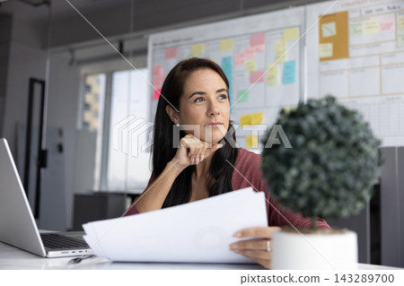 Professional woman hold analytical documents while thoughtfully looking into distance Professional woman hold analytical documents while thoughtfully looking into distance 143289700