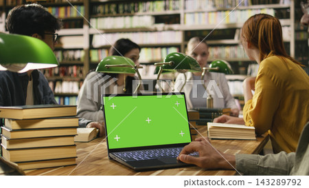 Chroma key isolated screen on laptop with student in over-the-shoulder shot, group study session in a library. Screen replacement with mockup near students at table. Chroma key isolated screen on laptop with student in over-the-shoulder shot, group study session in a library. Screen replacement with mockup near students at table. 143289792