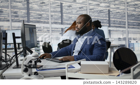 Examining microchip circuit layouts, computer monitor and man in factory RD office using specialized software. Improving manufacturing, semiconductors used in smart device sand African american worker Examining microchip circuit layouts, computer monitor and man in factory RD office using specialized software. Improving manufacturing, semiconductors used in smart device sand African american worker 143289820