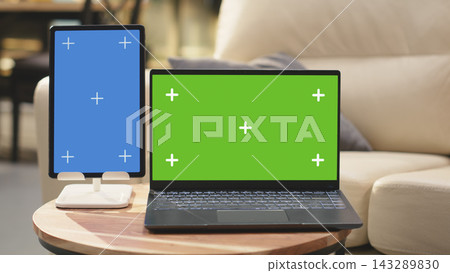 Green screen and vertical blue screen in home interior with coffee table, sunlit rustic wooden furniture. Two devices in open floor plan with warm tones, interior design with no people. 143289830